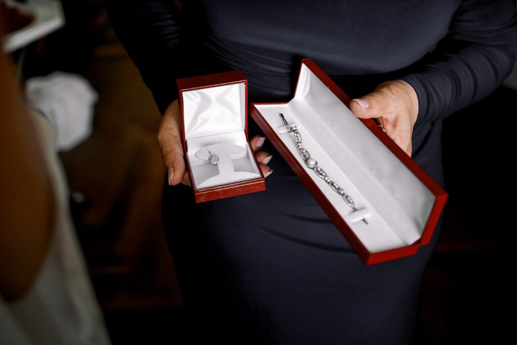 Värdering av smycken i dödsbo – så skrivs de in i bouppteckningen 2 Kvinna i mörk klänning håller i två smyckesaskar i röd sammet – en med ett örhänge i silver och en med ett diamantarmband.